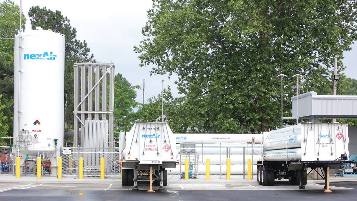 a gas filling plant with a very large gas cylinder with other horizontal gas cylinders on two semi truck trailer at the nexAir filling plant