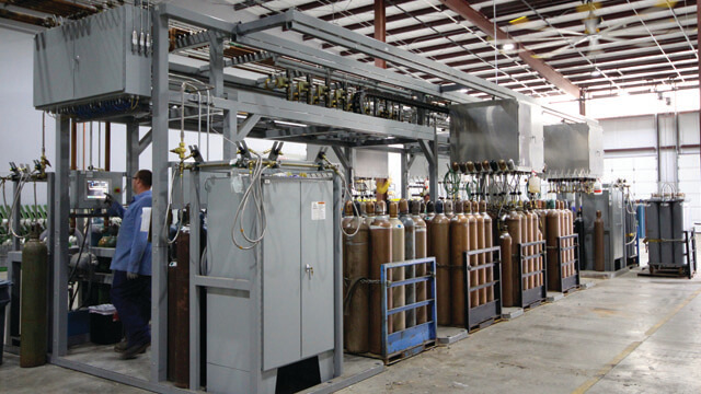 various gas cylinders in gas pallets next to or connected to gas cylinder filling equipment