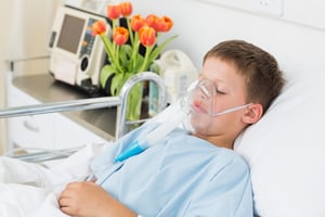 Sick little boy wearing oxygen mask in hospital ward