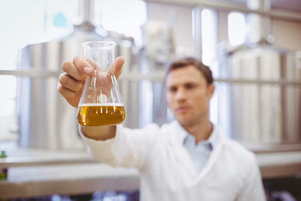 Thoughtful scientist holding a beaker in the factory